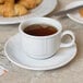 A Tuxton bright white china cup filled with tea on a plate.