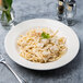 A Tuxton China pasta bowl filled with shrimp and garlic pasta on a table with a fork and knife.