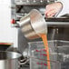 A chef using a Town tapered aluminum sauce pan to pour orange juice into a container.