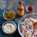 A bowl of shredded cabbage and carrots with a bowl of Cholula Chipotle hot sauce.