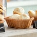 A dark brown Acopa woven plastic rattan bread basket filled with biscuits on a table.