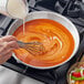 A hand using a whisk to stir white liquid in a bowl.