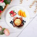 A Dart Concorde white foam plate with a muffin, orange slices, and berries on it.