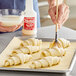 A person using Bake Sheen liquid to brush pastries before baking.