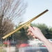 A hand using an Unger brass window squeegee to clean a window.