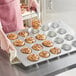 A woman holding a Baker's Mark Pecan Roll / Jumbo Muffin Pan with muffins in it.