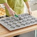 A person using a scoop to put batter in a Baker's Mark jumbo muffin pan.