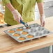 A person using a Baker's Mark jumbo crown muffin pan to put food into the cups.