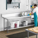 A man in a blue uniform using a Regency stainless steel dish table undershelf in a professional kitchen.