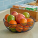A Tablecraft black wire square basket filled with oranges and a green apple.