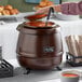 A person pouring soup into an Avantco copper soup kettle on a table.