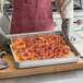 A person in an apron holding a rectangular pizza in an American Metalcraft perforated square pizza pan.