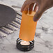 A hand holding an orange candle over a lit candle on a table.