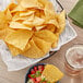 A bowl of Mejor Tortilla chips on a table with a glass of beer.