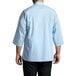 A man wearing a light blue Uncommon Chef 3/4 sleeve chef coat with side vents.