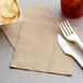 A fork and knife next to an EcoChoice natural kraft luncheon napkin.