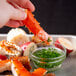 A hand holding a Chesapeake Crab Connection Alaskan King Crab leg with a bowl of sauce.