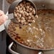 A metal measuring cup pouring Bossen Large Tapioca Pearls into a pot of boiling water.