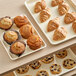 A Baker's Mark ivory non-stick metal tray filled with muffins and pastries on a counter.