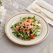 A WNA Comet ivory plastic plate with a gold accent band holding a salad with a fork and knife.