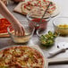 A person's hand reaching for cheese in an Anchor Hocking glass bowl of pizza ingredients.