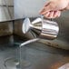 A hand holding a Town Asian Chef oil dispenser pouring oil into a pan.