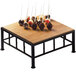 A Cal-Mil iron black square riser with a bamboo top on a wooden table with cake pops on skewers.