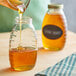 A person pouring honey into a Classic Queenline glass jar.