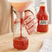 A person pouring red sauce into a glass BBQ sauce bottle.