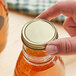 A person holding a 48/400 gold metal lid on a jar of liquid.