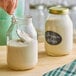 A person holding a spoon in a glass jar of white liquid.