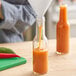 A close-up of orange liquid being poured into a 5 oz. glass Woozy bottle.