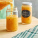 A person pouring orange liquid into a round glass jar.