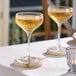 Two Acopa Silhouette coupe glasses on a table with yellow liquid.