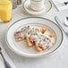 An Acopa ivory stoneware plate with green bands holding a meal with a glass of orange juice.