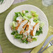 An Acopa Swell ivory stoneware plate with a wide rim and embossed design holding a chicken salad plate with a fork and knife.