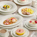 An Acopa Swell ivory stoneware plate with embossed wide rim on a table set with food and a cup of coffee.