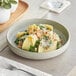 A white Acopa Pangea porcelain pasta bowl filled with pasta topped with cheese and nuts.