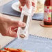 A person's hand using a Choice acrylic salt shaker and pepper mill to season a plate of fries.