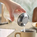 A glass sugar pourer with a metal lid being used to pour sugar into a cup of coffee.