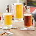 Two people holding Acopa paneled beer mugs full of beer on a table in a brewery tasting room.