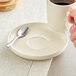 A hand holding a cup of coffee and a spoon on an Acopa Pangea fog white matte porcelain saucer.