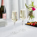 Two Acopa Silhouette champagne flutes on a table with a bottle of wine and a bouquet of flowers.