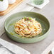 A sage green Acopa Pangea porcelain pasta bowl with spaghetti and cheese on a table.