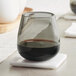 An Acopa Pangea stemless wine glass filled with dark liquid sits on a coaster on a table.