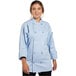 A woman wearing a sky blue Uncommon Chef long sleeve chef coat with buttons and pockets.