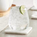 An Acopa Pangea stemless wine glass with ice and a slice of lime on a marble coaster.