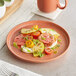 An Acopa Pangea Terra Cotta coupe plate with food on a table.