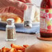 A hand holding a Choice mushroom top salt shaker over a plate of food with fries.