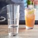 A person holding an Acopa Select 12 oz. highball glass filled with a drink, ice, and a lime wedge.